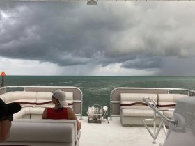 Guests relax on a boat as storm clouds gather over the ocean, creating a dramatic backdrop for a unique boating experience.