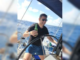 A man enjoys a refreshing drink while steering a sailboat, capturing the essence of a fun day on the water.