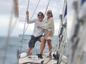 A joyful couple enjoys a sailing adventure on the open ocean, capturing a moment of fun and connection aboard their boat.