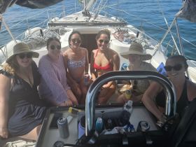 A lively group of friends enjoys a sunny day sailing, relaxing with drinks on board — perfect for a fun getaway on the water.