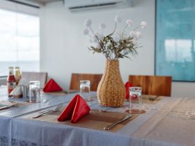 A beautifully set dining table inside a boat, featuring elegant red napkins and a decorative vase, perfect for onboard dining experiences.