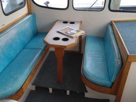 Interior view of a cozy boat cabin featuring comfortable seating and a table, perfect for dining or relaxing while on the water.