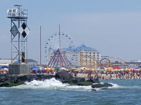 A vibrant beach scene featuring a bustling crowd enjoying summer activities, with a ferris wheel and amusement park in the background, perfect for family fun and seaside adventures.