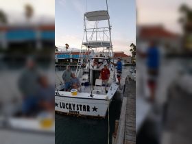 A lively group poses on the 'Lucky Star' fishing boat at the dock, ready for an exciting day on the water in Aruba.