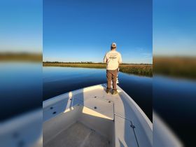 A fisherman stands at the bow of a boat, casting into calm waters surrounded by lush greenery — a perfect scene for a peaceful day of fishing.