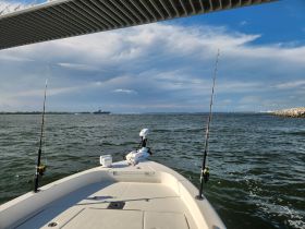 A scenic view from the bow of a fishing boat, showcasing the calm waters and a distant ship under a beautiful sky — perfect for a day of fishing adventures.