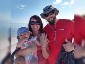 A joyful family poses on the beach, celebrating a special moment with a baby in arms — perfect for capturing cherished memories during a family outing.