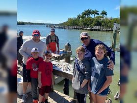 A joyful family poses with their catch of the day at the dock, celebrating a successful fishing trip together in beautiful weather.