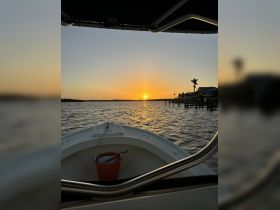 A serene sunset view from the bow of a boat, showcasing the tranquil waters and dockside scenery — perfect for evening cruises.
