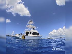 A stunning side view of a yacht cruising through clear blue waters, showcasing its sleek design against a backdrop of fluffy clouds.
