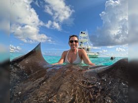 A woman joyfully interacts with a stingray in crystal-clear waters, showcasing a unique wildlife experience in the tropics.