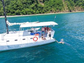 A lively group enjoys a day on a catamaran, with some swimming and snorkeling in the clear waters — a perfect day for adventure and relaxation.