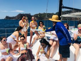 A lively group of women enjoys a festive day on a yacht, sipping cocktails and celebrating under the sun — perfect for bachelorette parties or summer getaways.