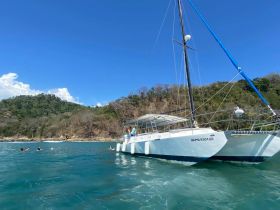 A lively scene featuring a group swimming near a catamaran, set against a stunning coastal backdrop — perfect for adventure seekers and beach lovers.