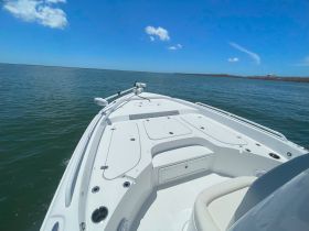 A clear view of the front deck of a speedboat cruising through calm waters, showcasing the vessel's sleek design against a vibrant blue sky.