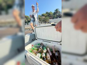 A cheerful guest enjoys the day on the boat, showcasing a cooler filled with a variety of drinks, perfect for a fun day on the water.