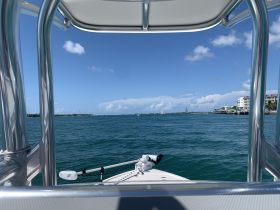 A clear view from the front of a boat cruising through turquoise waters, showcasing the scenic coastline and a bright blue sky.