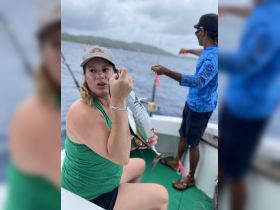 A woman proudly holds a freshly caught fish while fishing on a boat, showcasing the excitement of a fishing adventure on the open water.