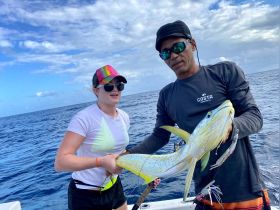 A young angler proudly holds a freshly caught fish alongside a guide, showcasing the excitement of fishing in the open ocean.