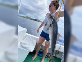 A woman proudly displays her catch while fishing on a boat, showcasing the thrill of deep-sea fishing adventures.