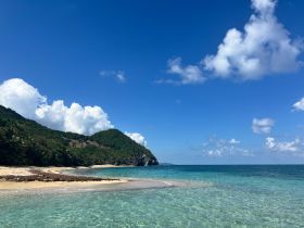 A stunning view of a serene beach with lush green hills and clear turquoise waters, perfect for a tropical getaway or island exploration.