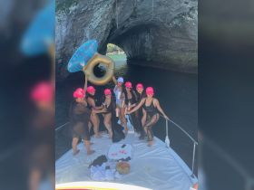 A lively group of friends celebrates a bachelorette party on a boat, complete with fun props and refreshments, creating unforgettable memories in a stunning coastal setting.