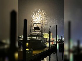 A stunning display of fireworks lights up the night sky over a marina, with a boat docked in the foreground, creating a festive atmosphere perfect for celebrations.