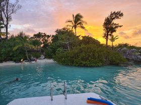 Children play on the beach as the sun sets over a tranquil lagoon, creating a picturesque scene perfect for family adventures and island exploration.