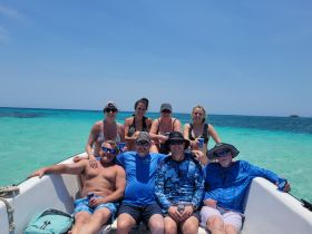 A lively group enjoys a day on the water, relaxing on a boat with drinks in hand against a stunning ocean backdrop — perfect for memorable outings and celebrations.
