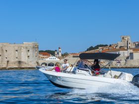 A group enjoys a scenic boat ride along the coastline, with historic architecture in the background, perfect for exploring beautiful destinations.