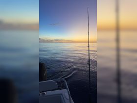 A serene sunset view from a fishing boat, showcasing calm ocean waters and a fishing rod poised for action — perfect for a peaceful evening on the water.
