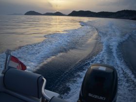 A serene view of a boat underway, leaving a wake in the calm waters at sunset, surrounded by distant islands — perfect for showcasing the beauty of boating in nature.