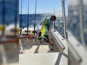 A proud angler showcases a vibrant mahi mahi catch aboard a fishing boat, capturing the thrill of deep-sea fishing in the open ocean.