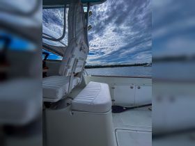 Interior view of a boat's helm and seating area, showcasing comfortable white upholstery and a scenic backdrop of water and clouds.