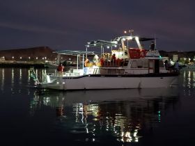 A lively scene at night with guests aboard a boat in the harbor, illuminated by lights reflecting on the water — perfect for evening cruises and social gatherings.