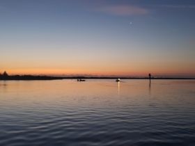 A serene sunset view over the water with boats in the distance, capturing the tranquil beauty of evening boating adventures.