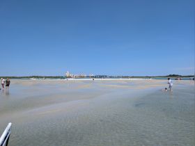 A family enjoys a sunny day at a sandbar, with children playing in the shallow water — a perfect spot for fun and relaxation on the beach.