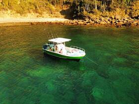 A group enjoys a fishing trip aboard a boat in crystal-clear waters, with a picturesque coastline in the background — perfect for adventure seekers.