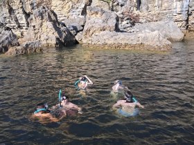 A group of snorkelers explores the clear waters near a rocky coastline, enjoying an adventurous day in nature.