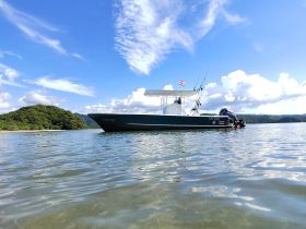 A fishing boat named 'Eagle Ray' is anchored in calm waters, with a scenic island backdrop and a person preparing fishing gear — perfect for adventure seekers and fishing enthusiasts.