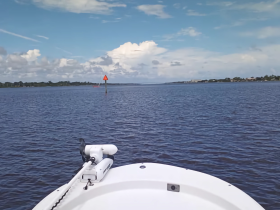 A clear view from the front of a boat navigating calm waters, showcasing the serene landscape and navigational marker ahead.