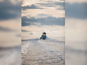 A boat speeds across the water with passengers onboard, creating a dynamic scene against a backdrop of dramatic clouds, perfect for adventure seekers on the open sea.