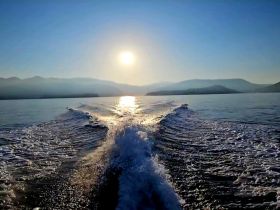 A stunning view of the sun setting over calm waters, showcasing the wake of a boat in motion — perfect for capturing the essence of a serene boating experience.