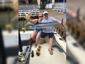 A couple proudly displays their impressive catch of the day, showcasing a large fish and lobster on a fishing trip — a perfect moment for fishing enthusiasts.