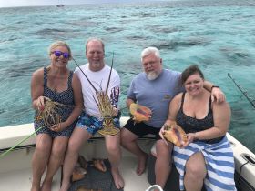 A cheerful group showcases their catch of lobsters and conch while enjoying a day on the water — a perfect highlight of a fishing adventure.