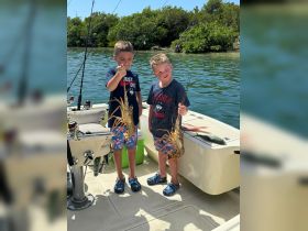 Two young boys proudly display their catch of lobsters while fishing on a boat, capturing a memorable moment of outdoor adventure and wildlife interaction.