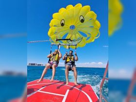 Two friends enjoy an exhilarating parasailing adventure over the sparkling blue waters, capturing the thrill of on-water activities.