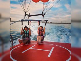 Two friends enjoy an exhilarating parasailing adventure over the water, capturing the thrill of on-water activities and group fun.