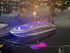 A sleek speedboat named 'Mr. Mitch' docked at night, illuminated by vibrant lights reflecting on the calm water — perfect for evening outings.