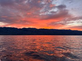 A breathtaking sunset paints the sky in vibrant hues over the mountains, creating a serene backdrop for unforgettable boating experiences.